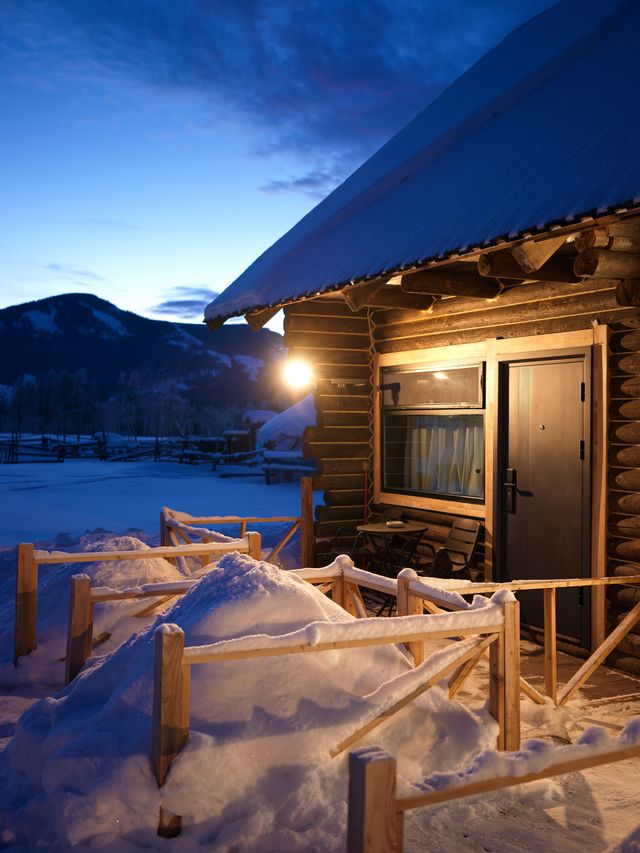 蓝色雪夜里木屋的窗灯与屋檐。