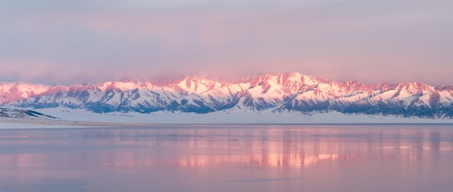 粉色光线中的雪山与湖面倒影全景。