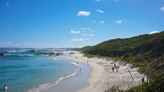 沙滩、绿色山坡与沿岸行走的人。