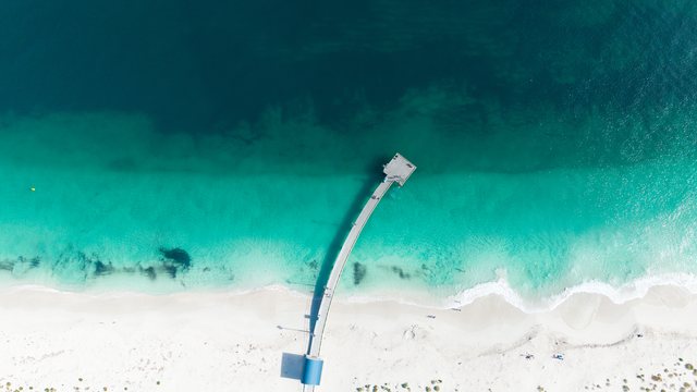 洁白沙滩、蓝绿色海水与细长栈桥航拍。
